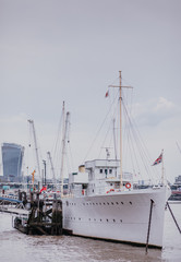 Naklejka premium beautiful white ship parked on the river Thames, bright sky above the river. Walkie Talkie building in the background. white metal ship with masts