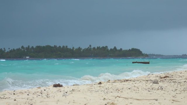 Small wooden boat rocks around in the rough seas with a storm approaching the empty white sand shoreline of Himmafushi. Raging tropical storm approaches a remote island in the Maldives. Rainy season