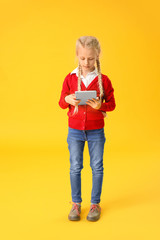 Cute little girl with tablet computer on color background. Concept of online education