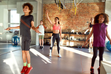 Perform better, be better. Full-length shot of female trainer controlling, looking after kids, while they are jumping rope in gym. Sport, healthy life, physical education concept