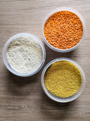 Three round plastic containers with dry food (flour, red lentils, couscous) sitting on wooden table. Top view, from above, flat lay.