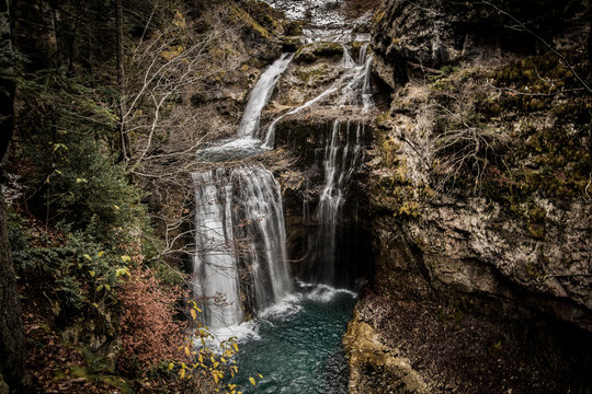 Cascada captada en larga exposici&oacute;n rodeada de rocas y vegetaci&oacute;n con el agua turquesa.