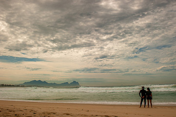 A couple watches the sea on the beach sands on a cloudy day.