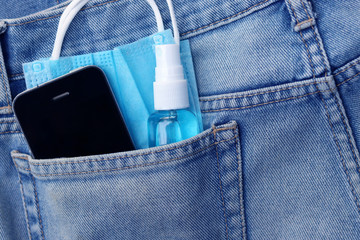 Medical face mask ,hand sanitizer spray and smart phone in jeans back pocket background. Concept...