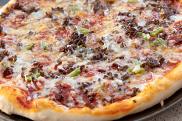 Homemade pizza fresh from the oven and unsliced.  Topped with pepperoni, cheese, peppers, onions, and beef.