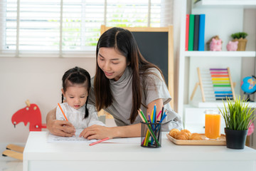 Asian kindergarten student girl with mother painting picture in book with color pencil at home, Homeschooling and distance learning..