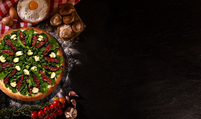 Tasty arugula and dried tomato pizza and cooking ingredients tomatoes basil on wood background. Top view of arugula pizza