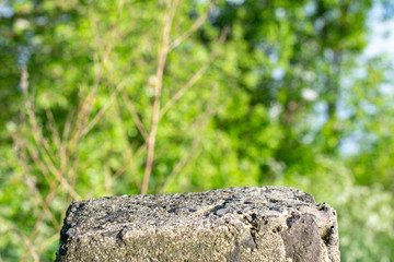 Standing old gray concrete pillar with planar surface on the top as a stage for something and blurred green grass background behind.