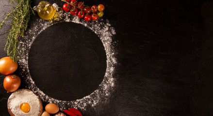 Various vegetables at black concrete background with copyspace on round pizza desk. Set of fresh vegetables. Egg, tomatoes, pepper, lettuce, onion, garlic, onion. Pizza ingredients.