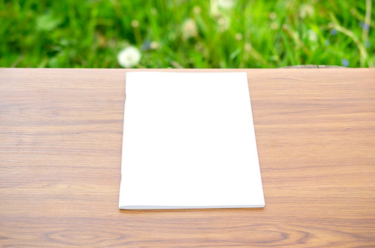 Clean and blank portrait magazine catalog on the wooden table with blurred green grass background behind as template for your design presentation, print promotion, portfolio etc.