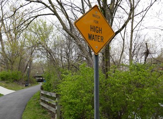 Public park nature walking path with high water caution sign