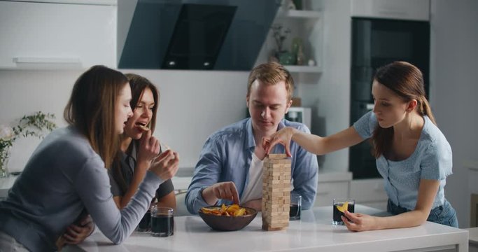 Friends are sitting in the kitchen and playing a board game of jenga. They talk and have fun, eat and drink. The concept of relaxation and entertainment.
