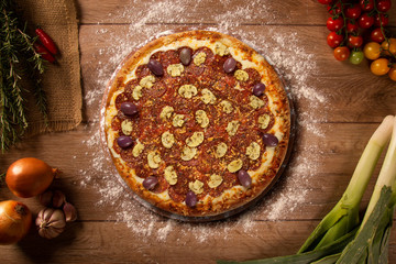 Tasty pepperoni and mushrooms pizza and cooking ingredients tomatoes basil on wood background. Top view of pepperoni pizza