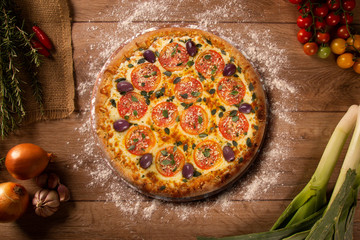 Tasty marguerita pizza and cooking ingredients tomatoes basil on wood background. Top view of marguerita pizza
