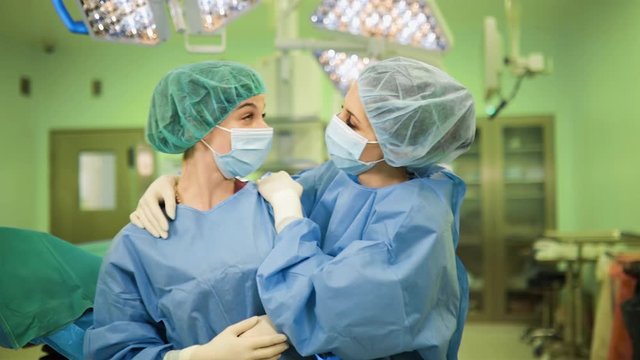 Happt female doctors after successful operation in medical face masks, gloves and caps in surgery operating hospital room
