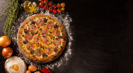 Tasty marguerita pizza and cooking ingredients tomatoes basil on black concrete background. Top view of marguerita pizza
