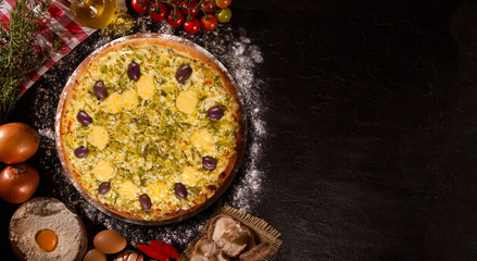 Tasty leek and mushrooms pizza and cooking ingredients tomatoes basil on black concrete background. Top view of leek pizza
