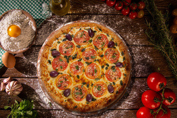 Tasty marguerita pizza and cooking ingredients tomatoes basil on wood background. Top view of...
