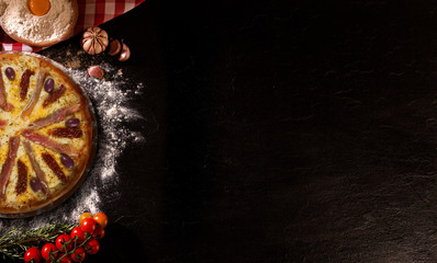Tasty prosciutto pizza and cooking ingredients tomatoes basil on black concrete background. Top view prosciutto pizza