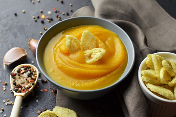 Butternut squash soup with croutons, fresh garlic and spices in ceramic bowl with spoon on grunge black background with linen napkin