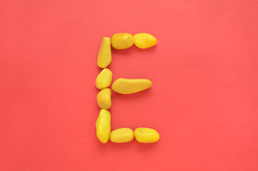 Letter E made of old Yellow pebbles on a red background