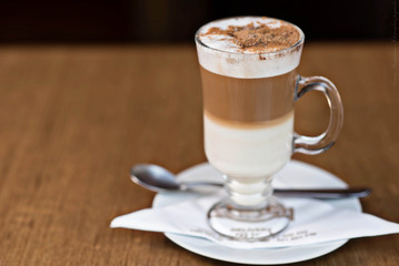 capuchino en un  vaso  y platito y una cuchara alado 