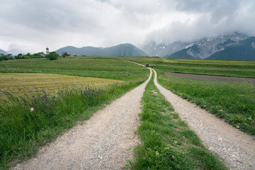 Tractor on a dirt road along farm fields with Austrian Alps, Mieminger Plateau, Tyrol, Austria