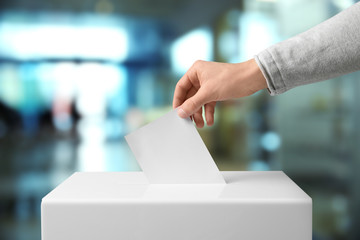 Man putting his vote into ballot box indoors, closeup