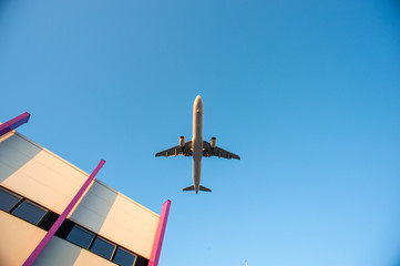 A passenger airplane on final approach flying over a warehouse building near the airport.