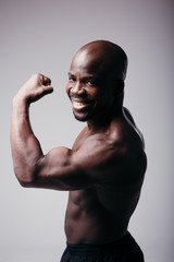 Plakat Portrait of a fitness trainer on gray background. Man shows biceps and smiles on a gray background