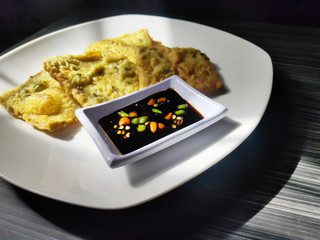 Tempeh or Tempe Mendoan with Soy Sauce and Chili on White Plate. Tempe Mendoan is Traditional Food From Indonesia. Blurry Background