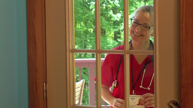 Closeup of mature woman nurse at home door knocking, showing badge, greeting, and entering.
