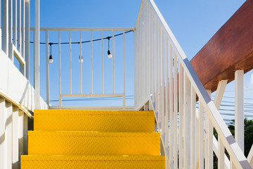 Yellow metal stairs with white corrugated wall and the hanging lights against the blue sky.