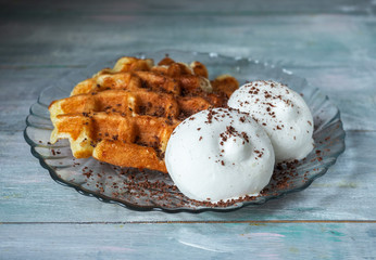 Tasty lunch with waffles and ice cream on a round glass plate standing on a wooden blue tray