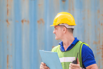 Happiness foreman in hardhat and safety vest talks on two-way radio, Worker man holding clipboard checklist at containers cargo