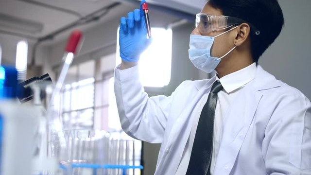 Asian cientist doing some research checking a liquid in a test tube at laboratory.
