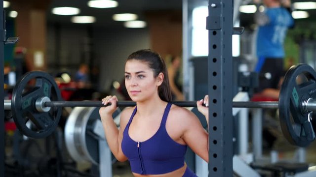 A beautiful athletic young brunette woman in sportswear in the gym performs exercises with a barbell. Fitness club.