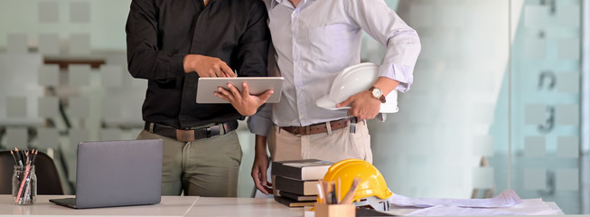 Cropped shot of two engineers working together with digital tablet, laptop and office supplies