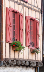 Windows with red shutters and geraniums on the wall of an ancient house