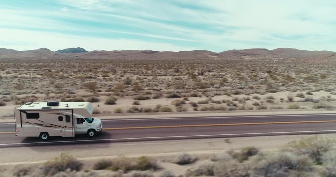 AERIAL - A drone follows an RV that drives at high speed through the image from left through right in the Mojave Desert on a sunny day