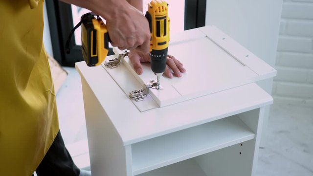 4k video of close up man holding cordless screwdriver machine and screws lie for screwing a screw assembling furniture at home....
