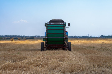 tractor makes big straw roll on yellow field at summer day