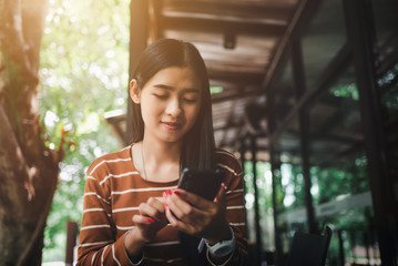 Portrait of asian happy woman at coffee shop and using mobile phone while sitting.