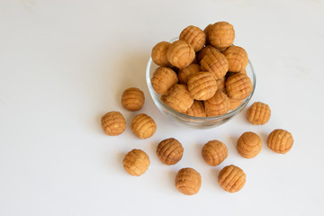 Round ruddy biscuit dainty dessert in the form of small balls. Cookies are in a transparent glass bowl and are scattered nearby on a white table.