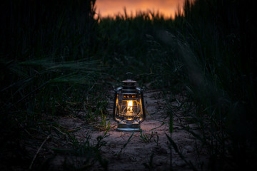 burning lantern stands in a cornfield at dusk - obrazy, fototapety, plakaty