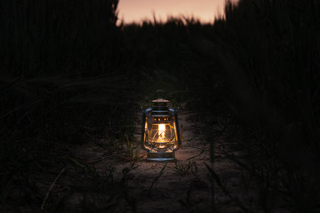 burning lantern stands in a cornfield at dusk © karegg