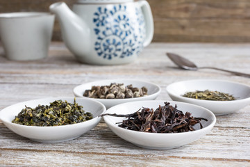 A closeup view of several condiment saucers filled with a variety of dried loose leaf tea, on a rustic wooden table surface.