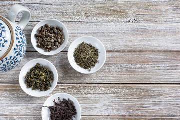 A top down view of several condiment saucers filled with a variety of dried loose leaf tea, on a rustic wood table surface.
