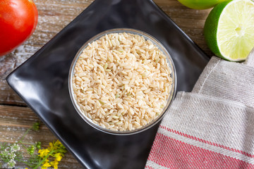 A top down view of a glass bowl of brown rice, in a still life setting.