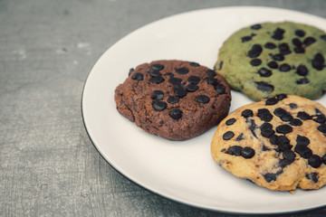 various chocolate cookies on white plate on grey cement surface